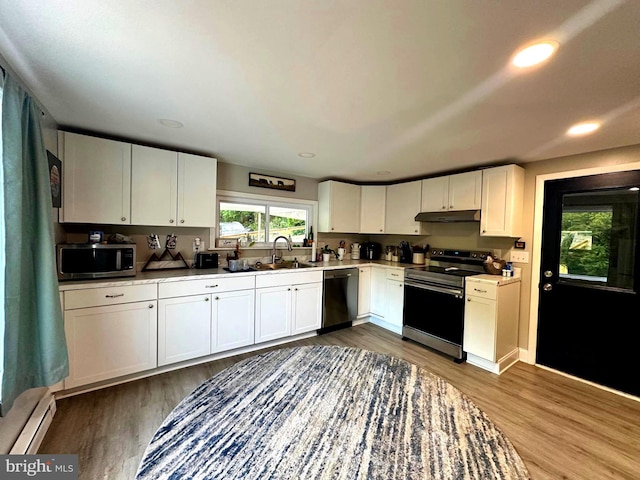 kitchen featuring under cabinet range hood, stainless steel appliances, baseboard heating, and dark wood-style floors