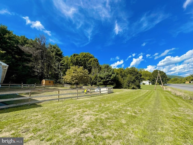 view of yard featuring an outdoor structure, a rural view, and fence