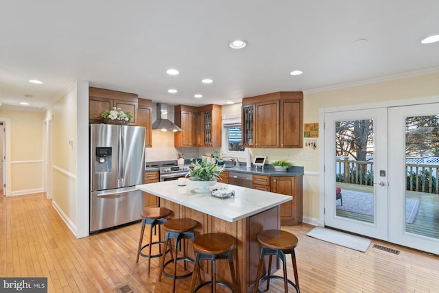 kitchen with wall chimney range hood, brown cabinetry, visible vents, appliances with stainless steel finishes, and a kitchen breakfast bar