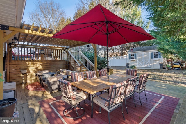 wooden terrace featuring an outbuilding, fence, a shed, outdoor dining area, and a pergola