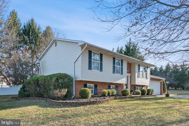 bi-level home with brick siding, a front lawn, fence, driveway, and an attached garage