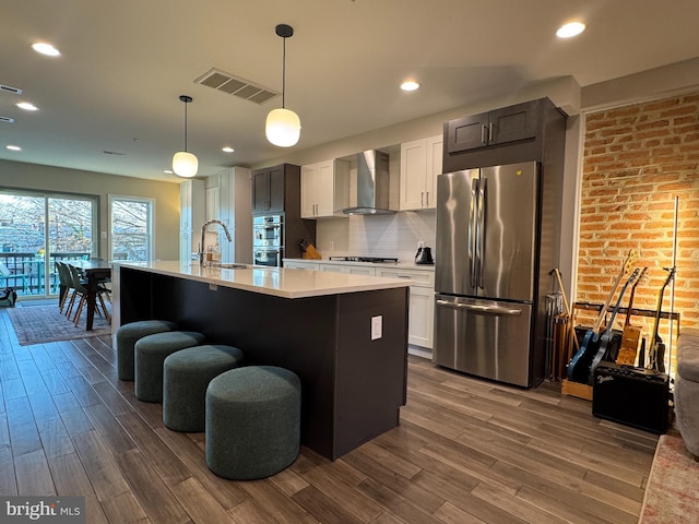 kitchen with visible vents, wall chimney range hood, light countertops, appliances with stainless steel finishes, and dark wood-style floors