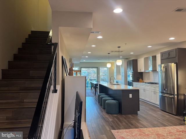 kitchen with dark wood-style floors, visible vents, appliances with stainless steel finishes, and wall chimney range hood