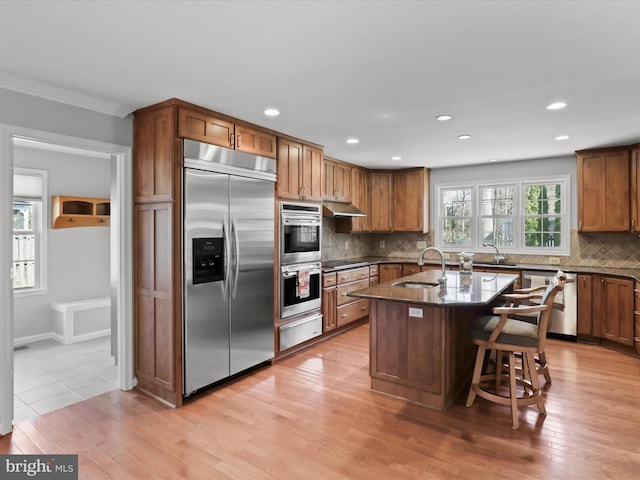 kitchen with light wood-style flooring, a sink, stainless steel appliances, under cabinet range hood, and a warming drawer