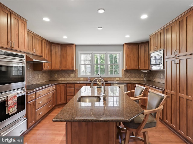 kitchen with a breakfast bar area, brown cabinetry, stainless steel appliances, a warming drawer, and a sink