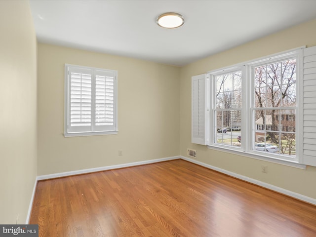 spare room featuring baseboards, plenty of natural light, visible vents, and wood finished floors