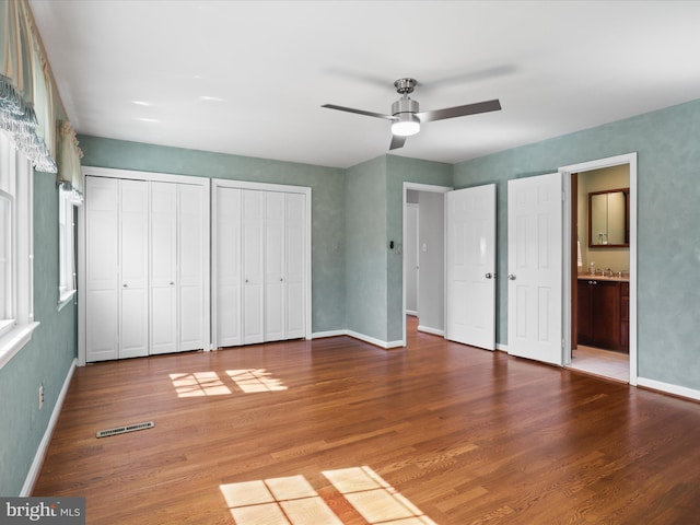 unfurnished bedroom with baseboards, two closets, ensuite bath, and wood finished floors