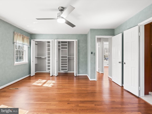 unfurnished bedroom featuring visible vents, two closets, wood finished floors, baseboards, and ceiling fan