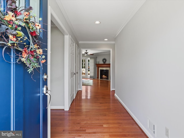 entrance foyer with crown molding, baseboards, recessed lighting, a warm lit fireplace, and wood finished floors