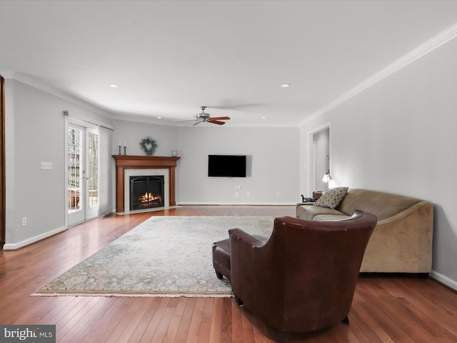 living area with a fireplace with flush hearth, crown molding, baseboards, and wood-type flooring