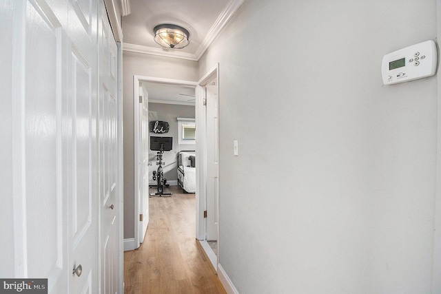 hallway with light wood-type flooring, crown molding, and baseboards