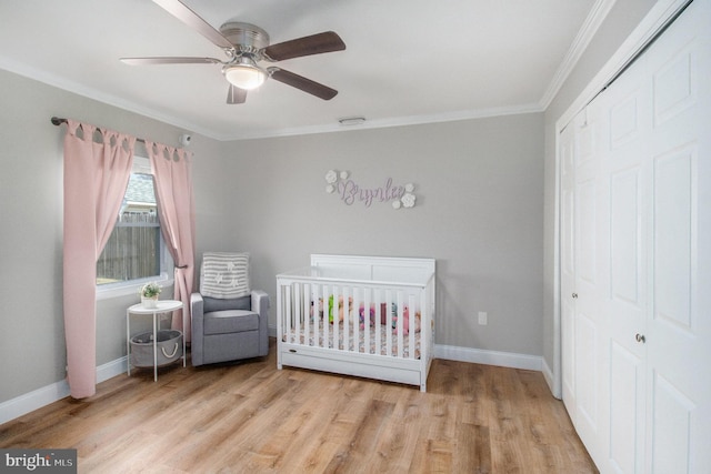 bedroom with light wood finished floors, crown molding, baseboards, a closet, and a nursery area