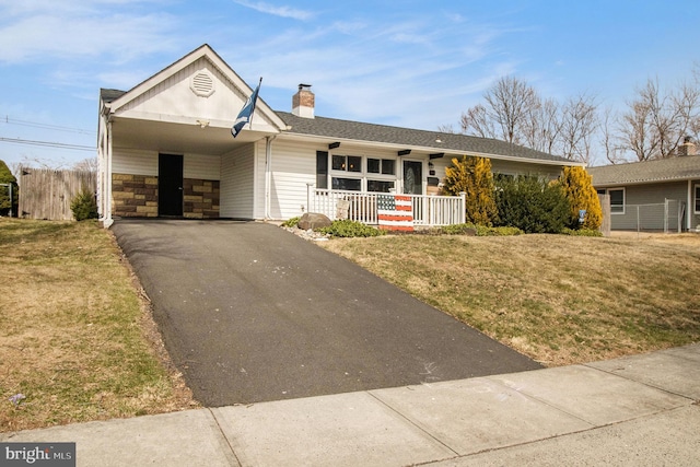 ranch-style house featuring a front lawn, aphalt driveway, covered porch, a chimney, and a carport