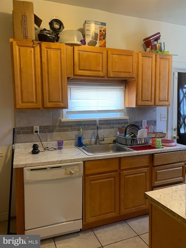 kitchen featuring light tile patterned flooring, white dishwasher, a sink, light countertops, and tasteful backsplash