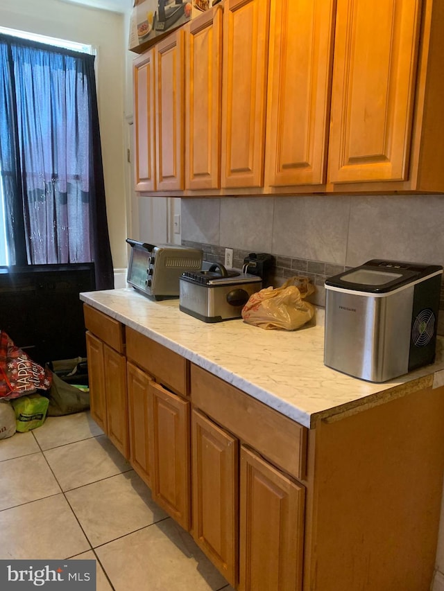 kitchen featuring tasteful backsplash, light tile patterned flooring, brown cabinetry, and a toaster