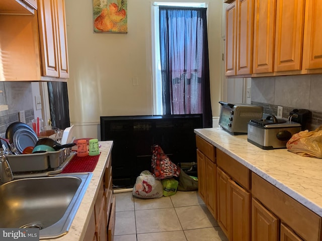 kitchen with a sink, backsplash, light tile patterned flooring, brown cabinetry, and a toaster