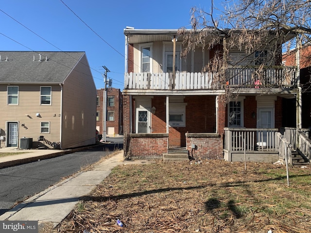 multi unit property with central AC unit, brick siding, covered porch, and a balcony