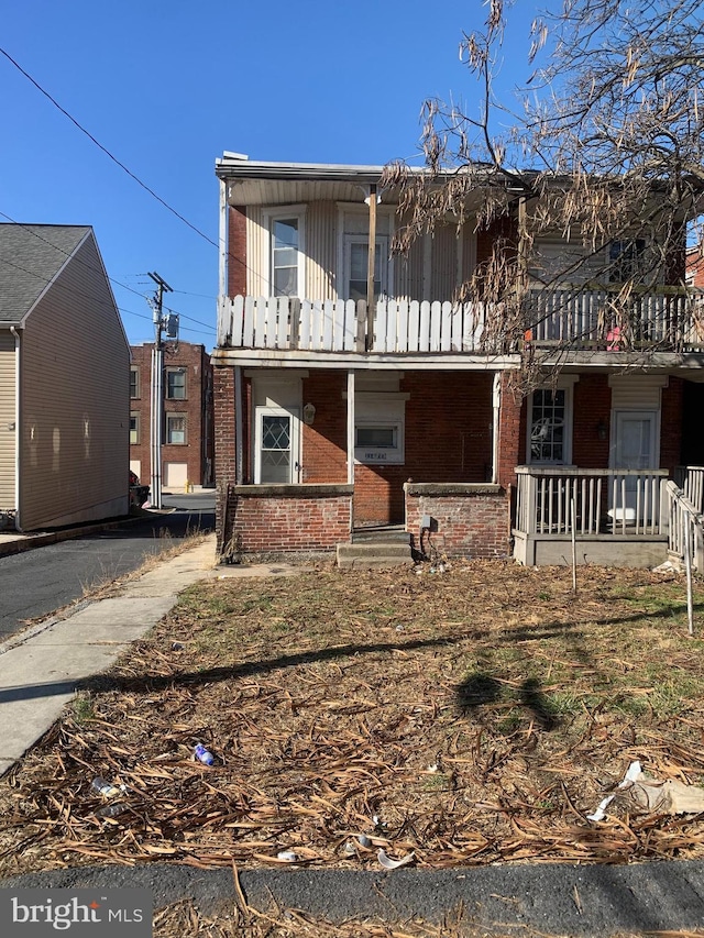 view of front facade with a balcony, covered porch, and brick siding