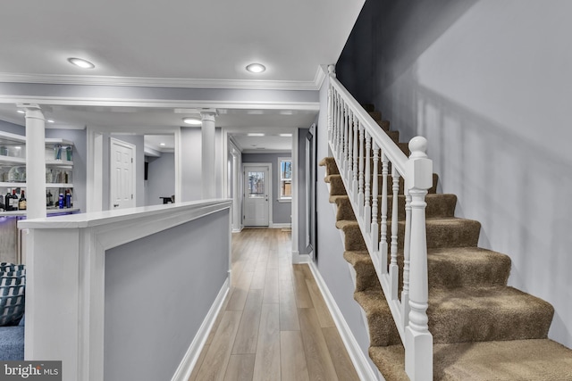 stairs with decorative columns, baseboards, wood finished floors, and crown molding