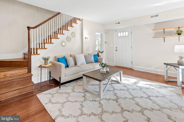 living area featuring stairway, baseboards, visible vents, and wood finished floors