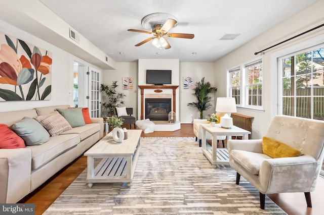 living room with visible vents, wood finished floors, a glass covered fireplace, and a ceiling fan