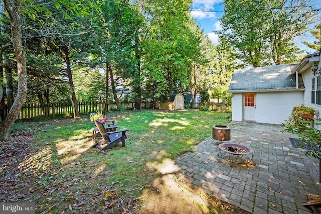 view of yard featuring a patio, a fenced backyard, an outdoor structure, a storage unit, and a fire pit