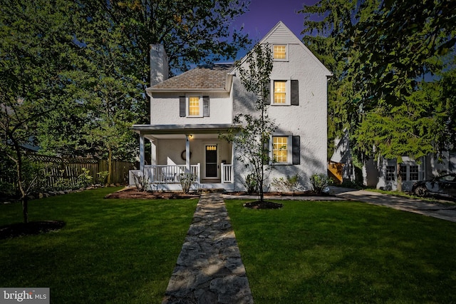 view of front of house featuring a front lawn, fence, stucco siding, covered porch, and a chimney