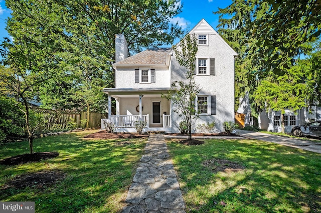 view of front facade with fence, a front yard, stucco siding, covered porch, and a chimney