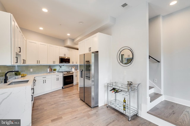 kitchen with tasteful backsplash, light wood-type flooring, light stone counters, appliances with stainless steel finishes, and a sink