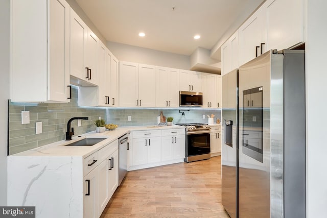 kitchen featuring a sink, tasteful backsplash, white cabinetry, stainless steel appliances, and light wood-style floors