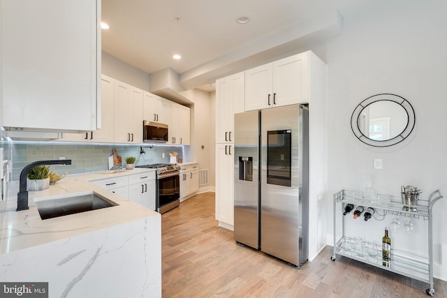 kitchen featuring white cabinets, light stone counters, appliances with stainless steel finishes, and a sink