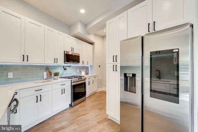 kitchen with visible vents, tasteful backsplash, white cabinetry, stainless steel appliances, and light wood-style floors