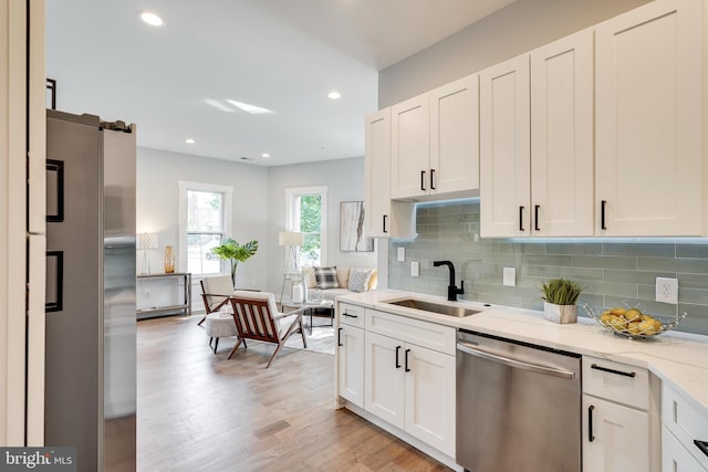 kitchen with light stone counters, light wood-style flooring, a sink, decorative backsplash, and stainless steel appliances