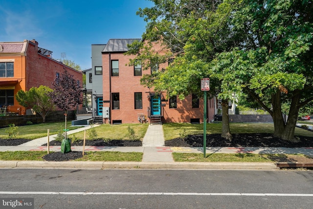 townhome / multi-family property featuring a standing seam roof, a front lawn, brick siding, and metal roof