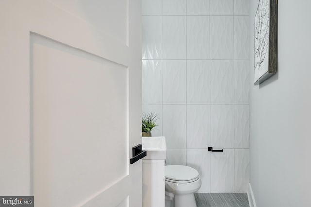 bathroom with toilet and tile walls