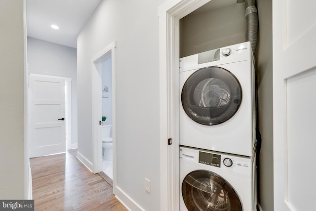 clothes washing area featuring light wood finished floors, baseboards, laundry area, recessed lighting, and stacked washer / drying machine