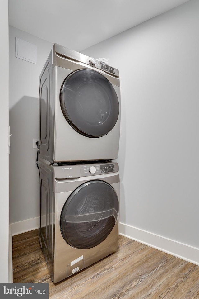 laundry room featuring laundry area, wood finished floors, stacked washer / drying machine, and baseboards