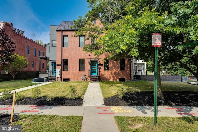 townhome / multi-family property featuring a standing seam roof, a front yard, brick siding, and metal roof