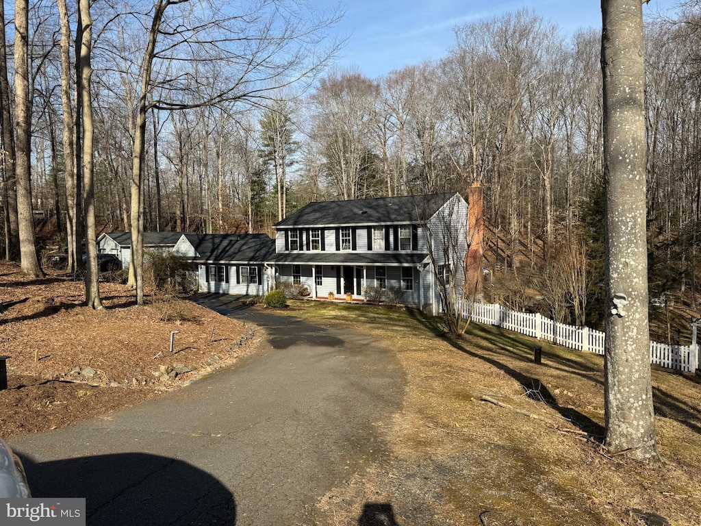 view of front facade featuring aphalt driveway, covered porch, and fence