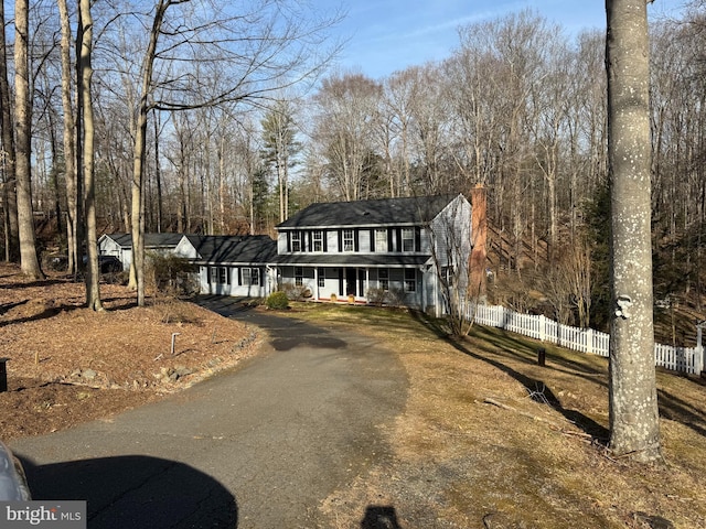 view of front facade featuring aphalt driveway, covered porch, and fence