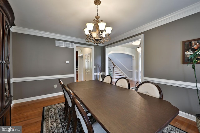 dining space featuring wood finished floors, baseboards, visible vents, arched walkways, and a chandelier