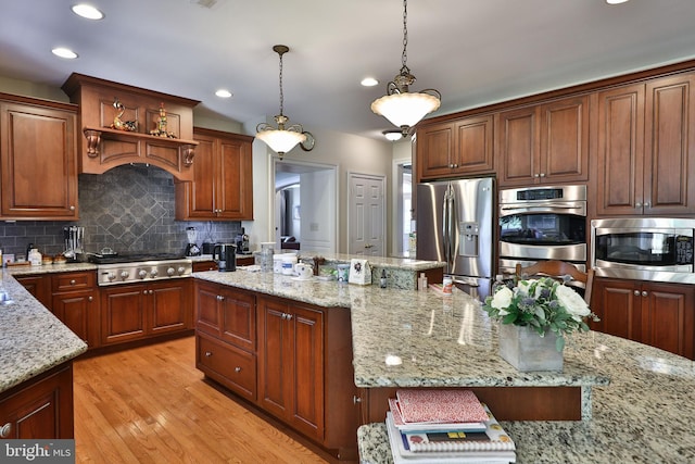 kitchen with light stone countertops, stainless steel appliances, hanging light fixtures, light wood-style floors, and backsplash