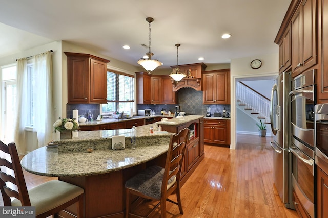 kitchen with light wood finished floors, a center island, pendant lighting, a breakfast bar, and light stone counters