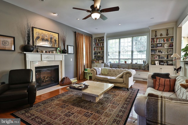 living area featuring built in shelves, a ceiling fan, wood finished floors, recessed lighting, and a fireplace