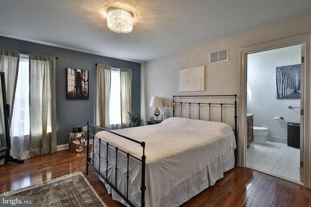 bedroom with visible vents, a notable chandelier, hardwood / wood-style flooring, ensuite bath, and baseboards