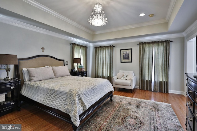 bedroom featuring wood finished floors, baseboards, a tray ceiling, ornamental molding, and a chandelier