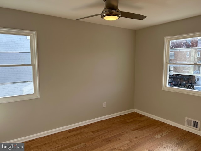 empty room featuring wood finished floors, a healthy amount of sunlight, visible vents, and baseboards