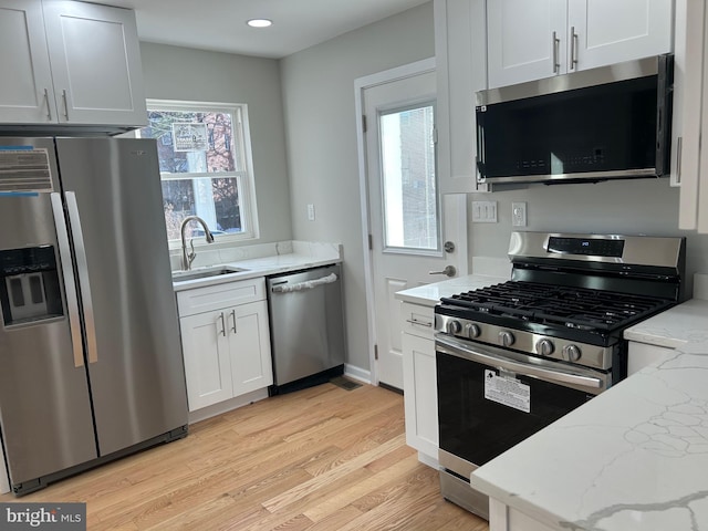 kitchen featuring a sink, light stone counters, light wood-style floors, appliances with stainless steel finishes, and white cabinets