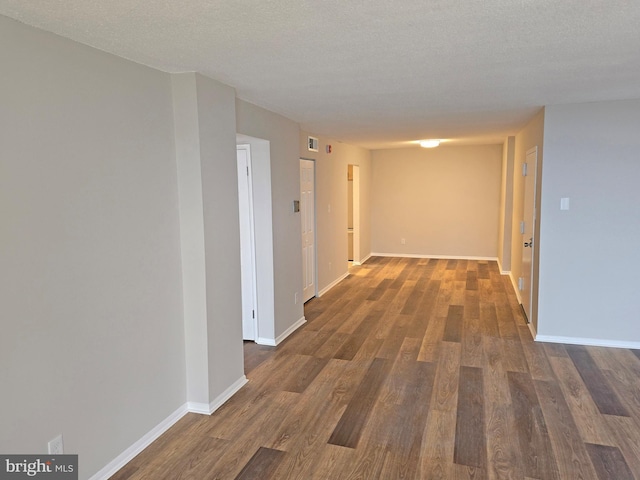 hall featuring visible vents, a textured ceiling, baseboards, and wood finished floors