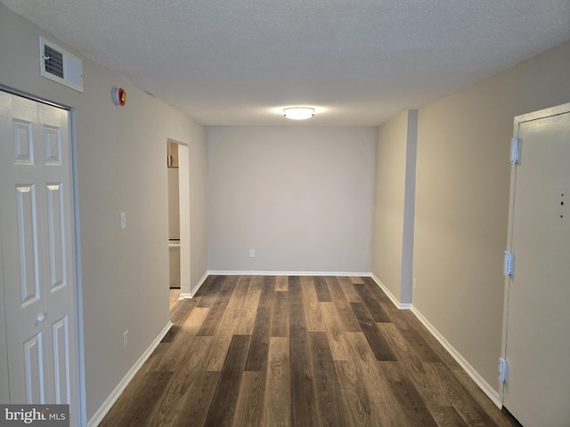 hallway with dark wood-style floors, visible vents, a textured ceiling, and baseboards